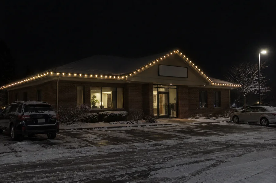 Small brick office building at night with warm white C9 Christmas lights along the roofline