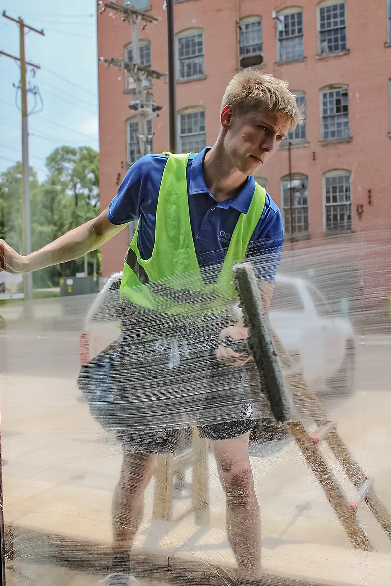 Go To Cleaning technician squeegeeing a large storefront window, seen through the glass