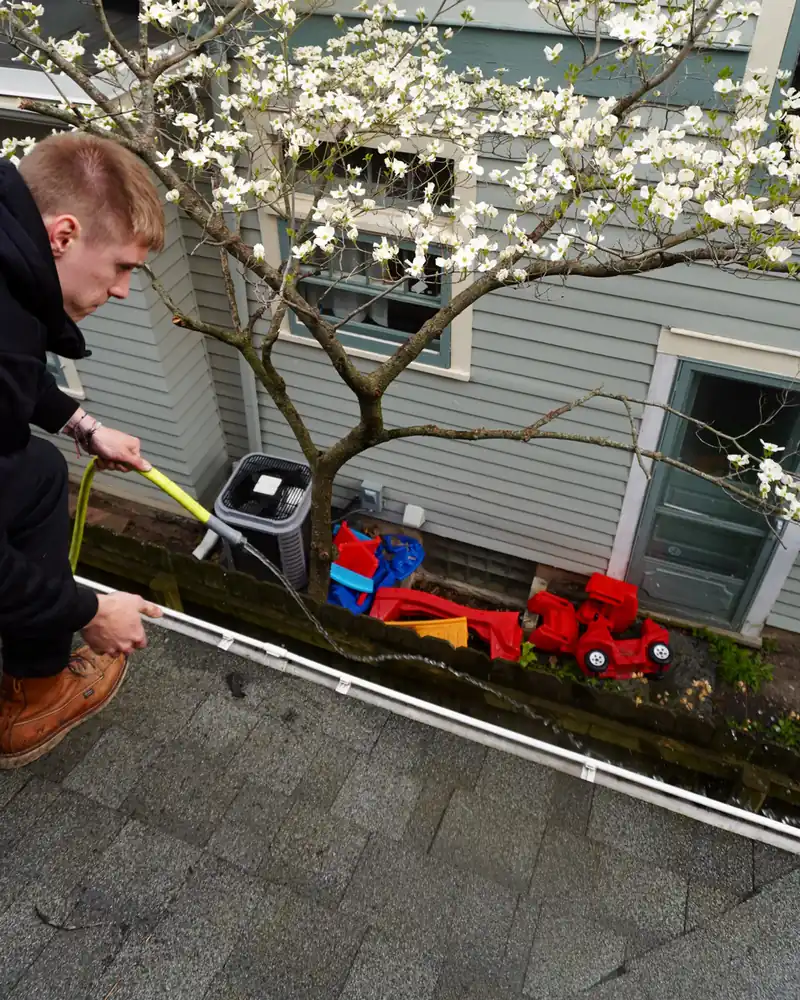 Go To Cleaning technician cleaning gutters by hand from the roof under a blooming dogwood