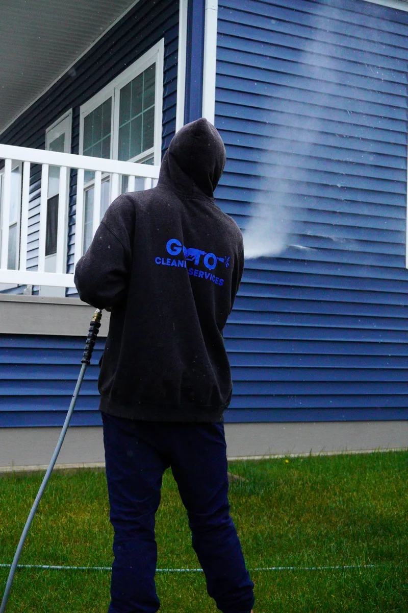 Go To Cleaning technician soft washing blue vinyl siding on a Rockford home