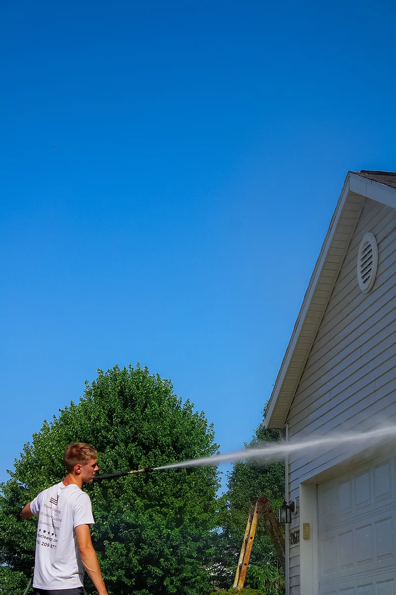 Go To Cleaning technician soft washing the peak of a home from the driveway