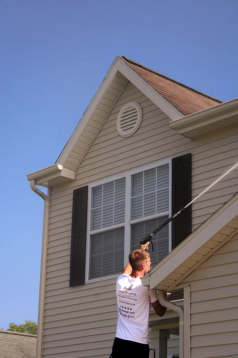 Go To Cleaning technician soft washing vinyl siding below a gable