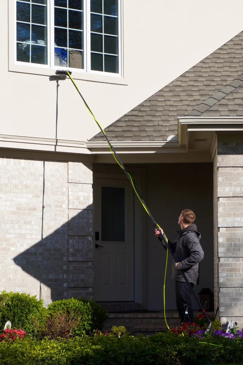 Go To Cleaning technician using a water-fed pole to clean second-story windows on a West Michigan home
